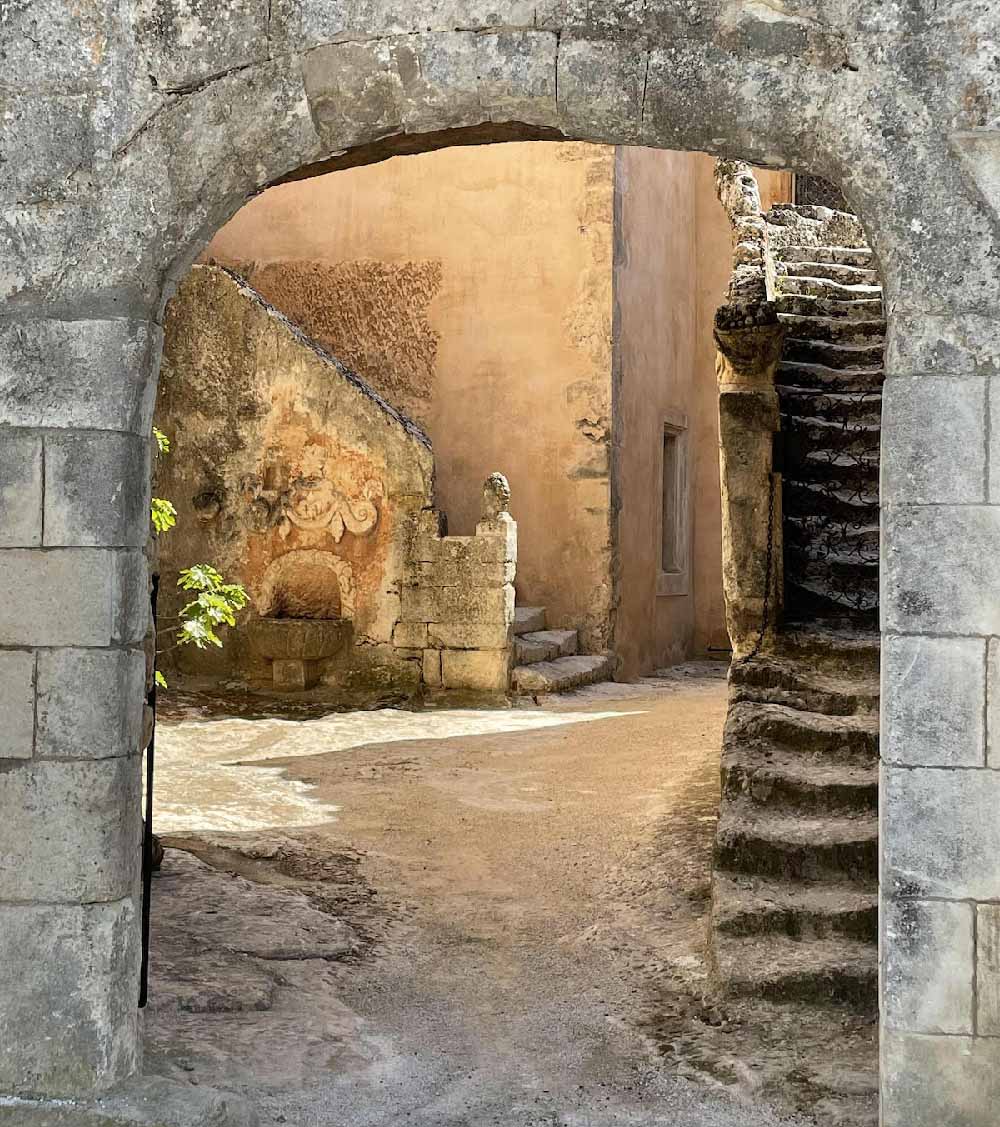 Porche en pierre donnant sur une cour pittoresque avec un escalier ancien au Château de Mille à Apt.