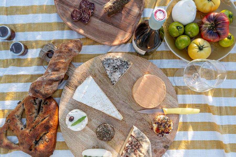 Plateau de fromages de chèvre artisanaux avec pain, vin et légumes de saison sur nappe rayée