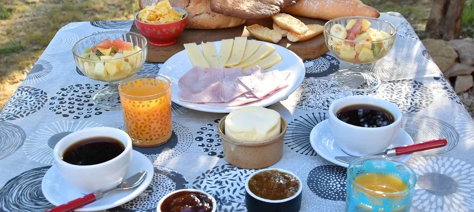 Petit-déjeuner maison en extérieur avec boissons chaudes, fruits, fromages et confitures