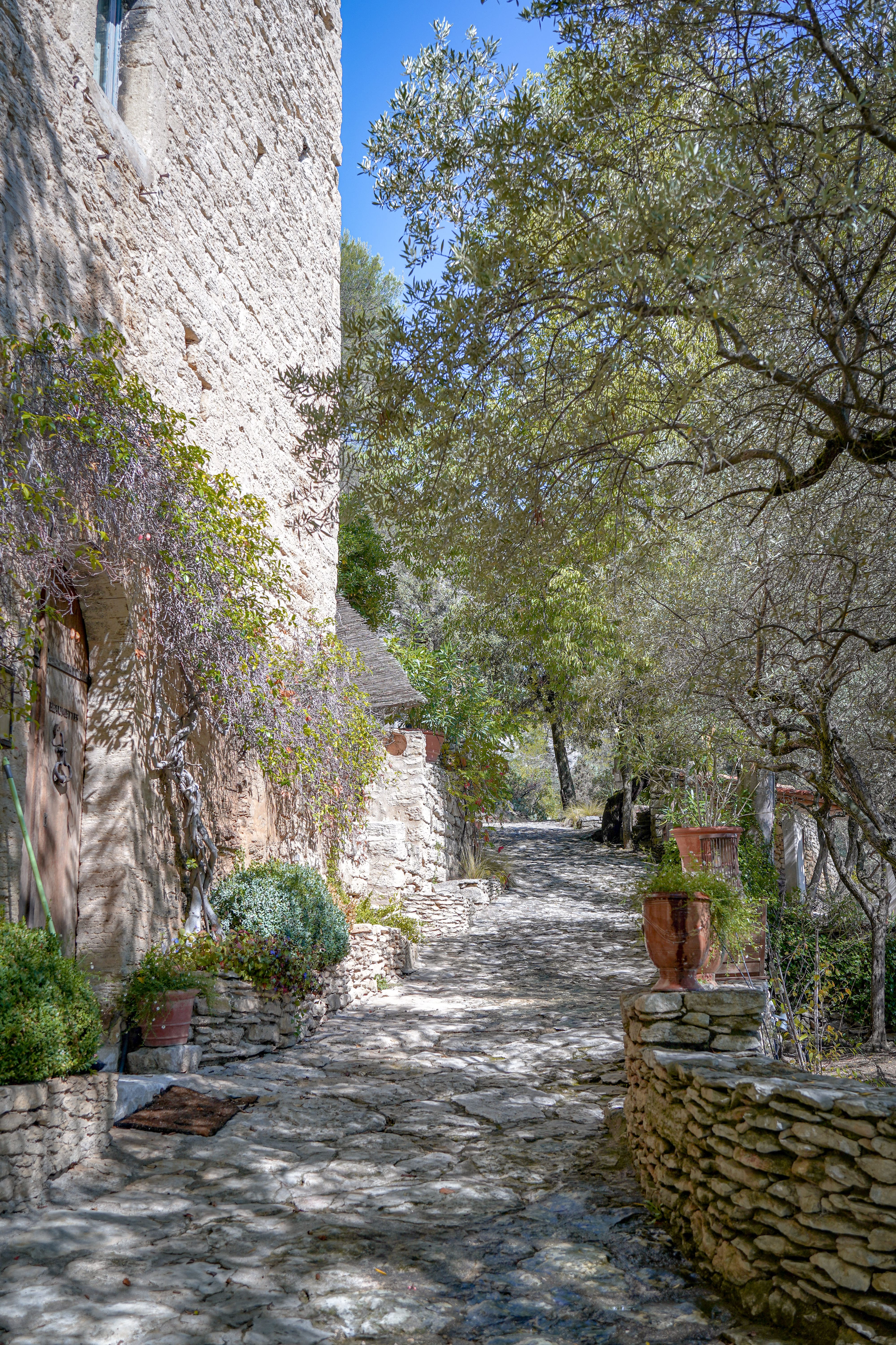 Chemin pavé bordé de murs en pierre et de végétation aux Beaumettes, au cœur du Luberon