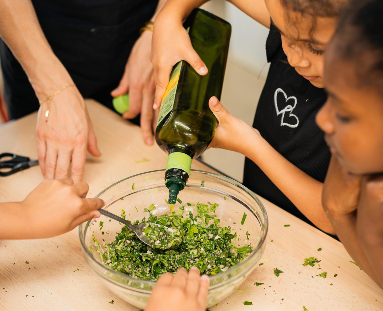 Enfants préparant une recette avec des herbes fraîches et de l’huile lors d’un atelier cuisine autour des saveurs au Festival Confit !