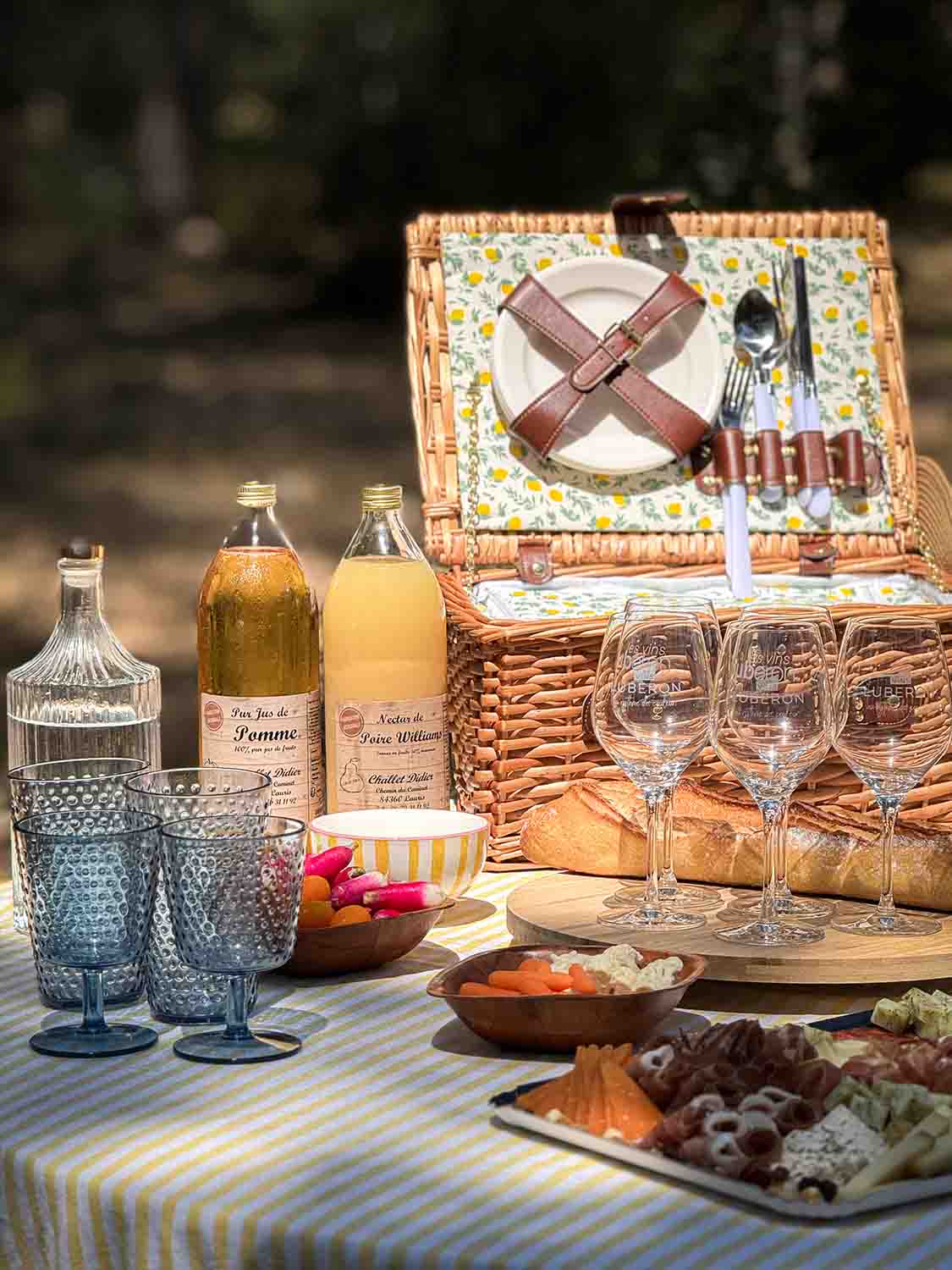 Panier de pique-nique en osier garni avec verres et bouteilles sur une nappe à carreaux