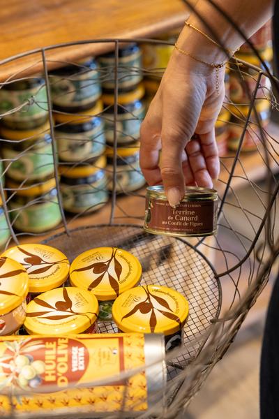 Main prenant un produit gourmand dans un panier aux Délices du Luberon
