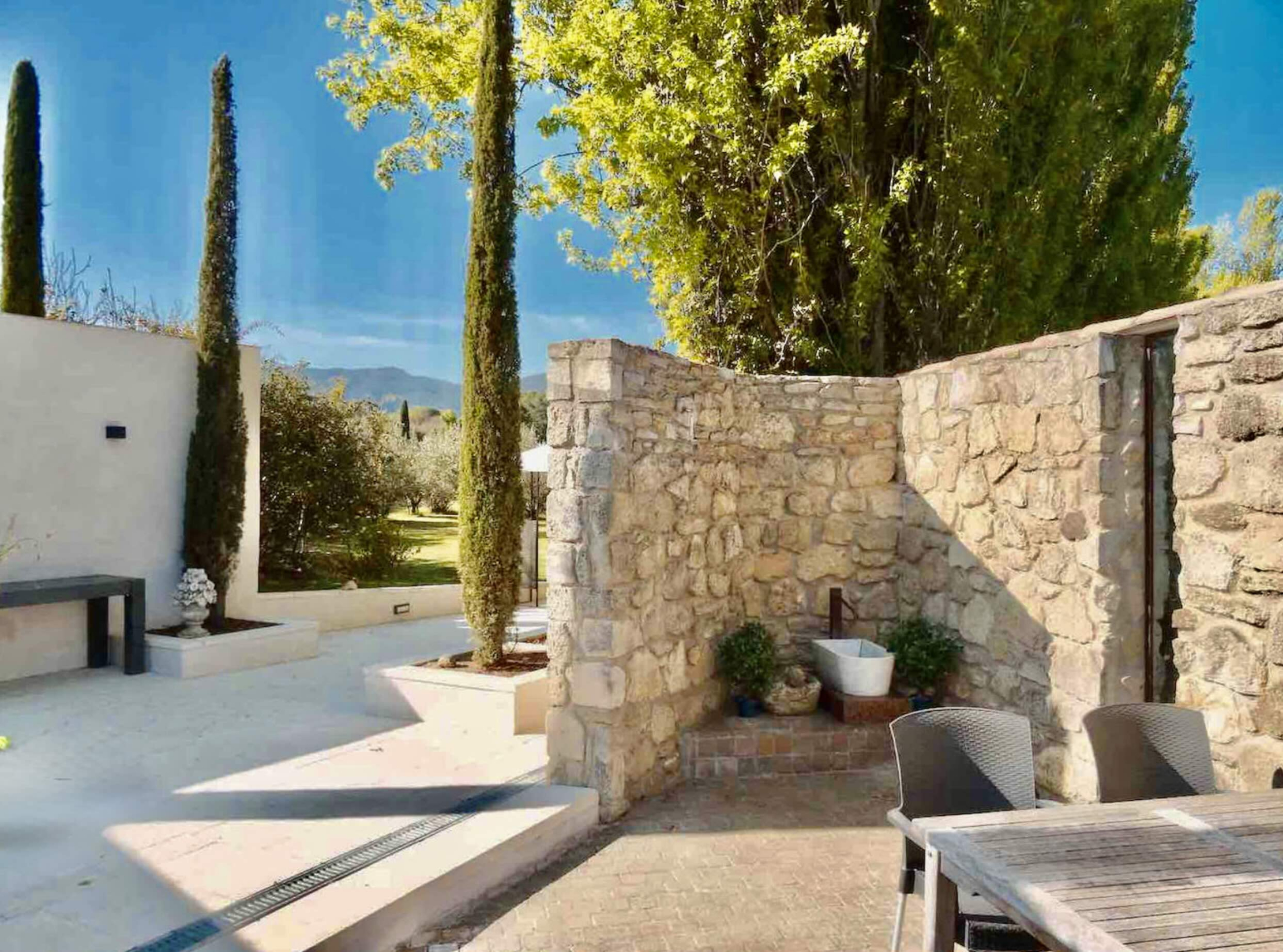 Terrasse privative et architecture provençale, maison Les Oliviers à Oppède Terrasse privative de la maison Les Oliviers à Oppède, avec murs en pierre, cyprès et espaces de détente, dans un cadre paisible du Luberon