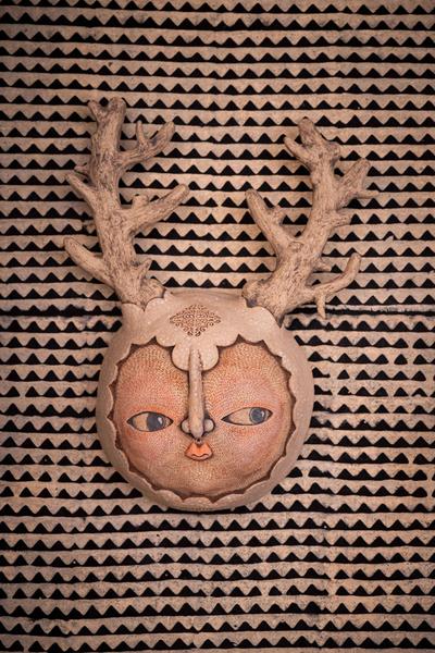 Sculpture murale en céramique représentant un visage surmonté de bois de cerf
