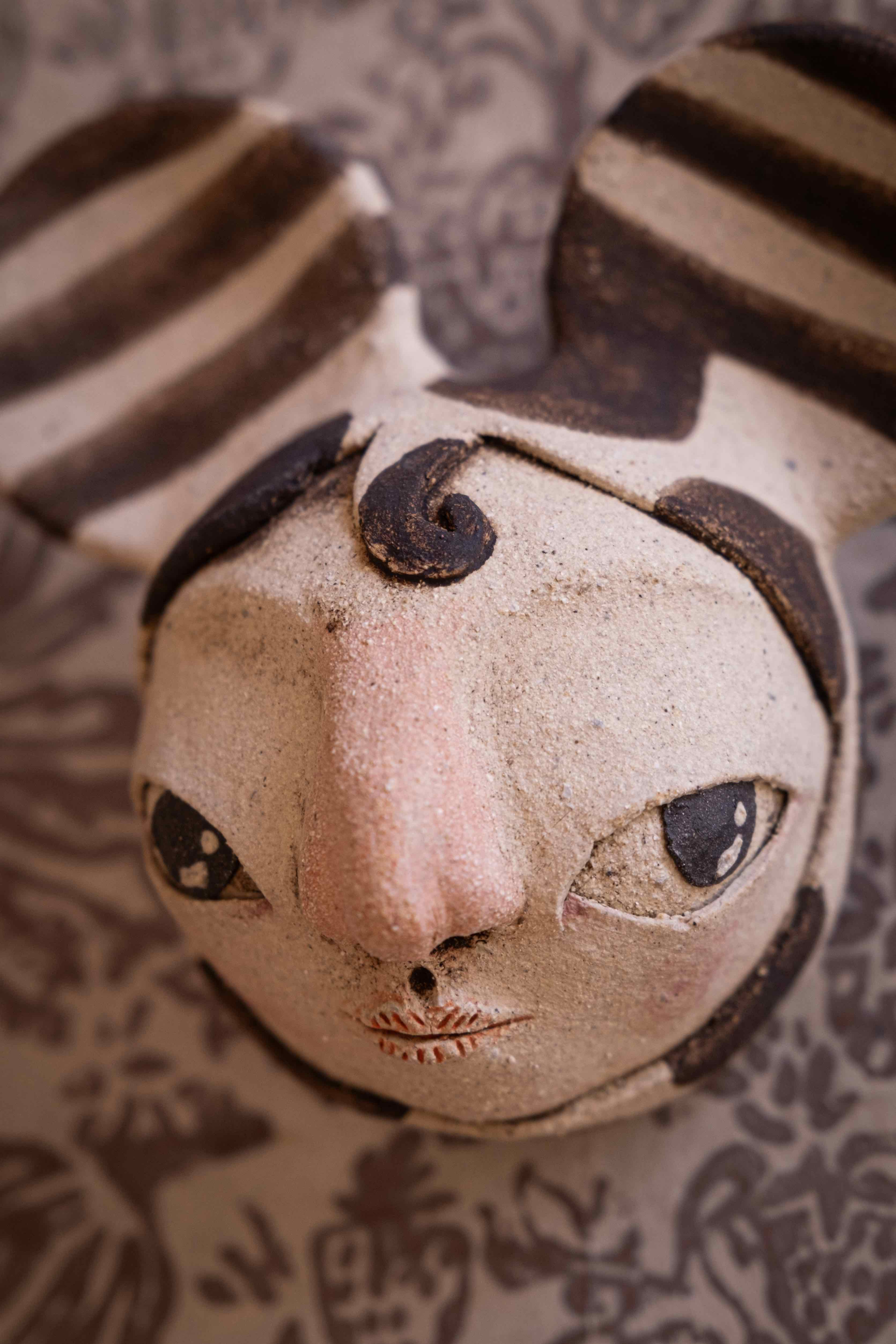 Détail d'un visage sculpté en céramique, aux yeux étirés et aux motifs bruns