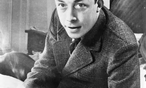 Albert_Camus,_gagnant_de_prix_Nobel,_portrait_en_buste,_posé_au_bureau,_faisant_face_à_gauche,_cigarette_de_tabagisme.jpg