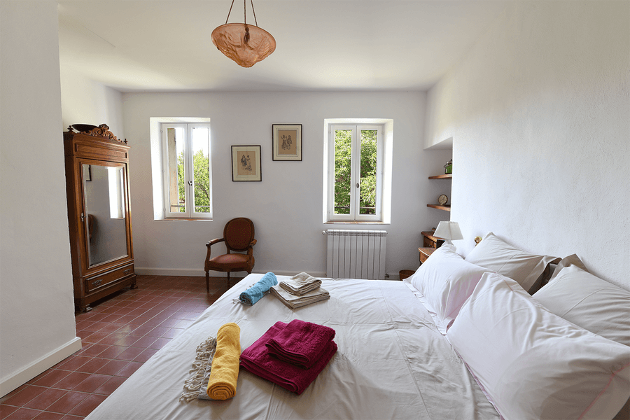 Chambre lumineuse et élégante du Mas du Péressier, avec un lit double, des serviettes colorées et une armoire ancienne.