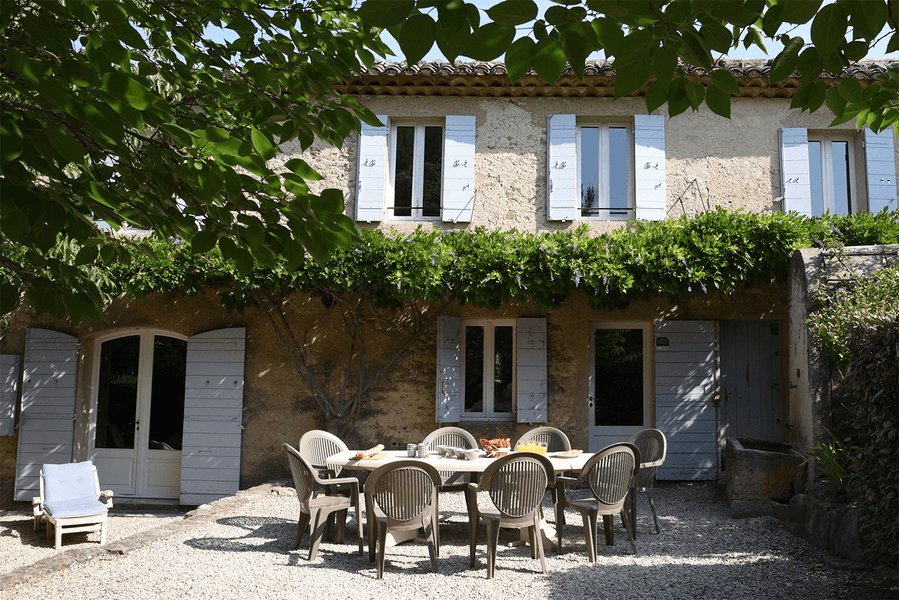 Cour extérieure du Mas du Péressier, avec une grande table en plein air sous une tonnelle de verdure, dans un cadre typique du Luberon.
