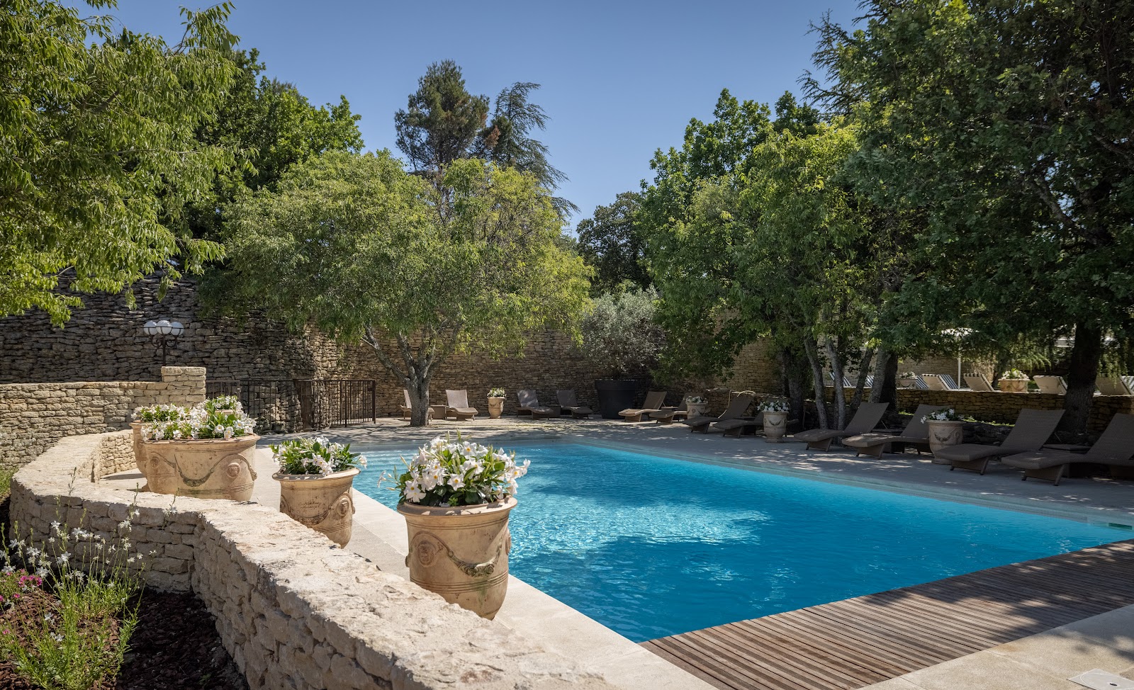 Piscine extérieure de l’hôtel Le Jas de Gordes entourée de murs en pierre et d’arbres