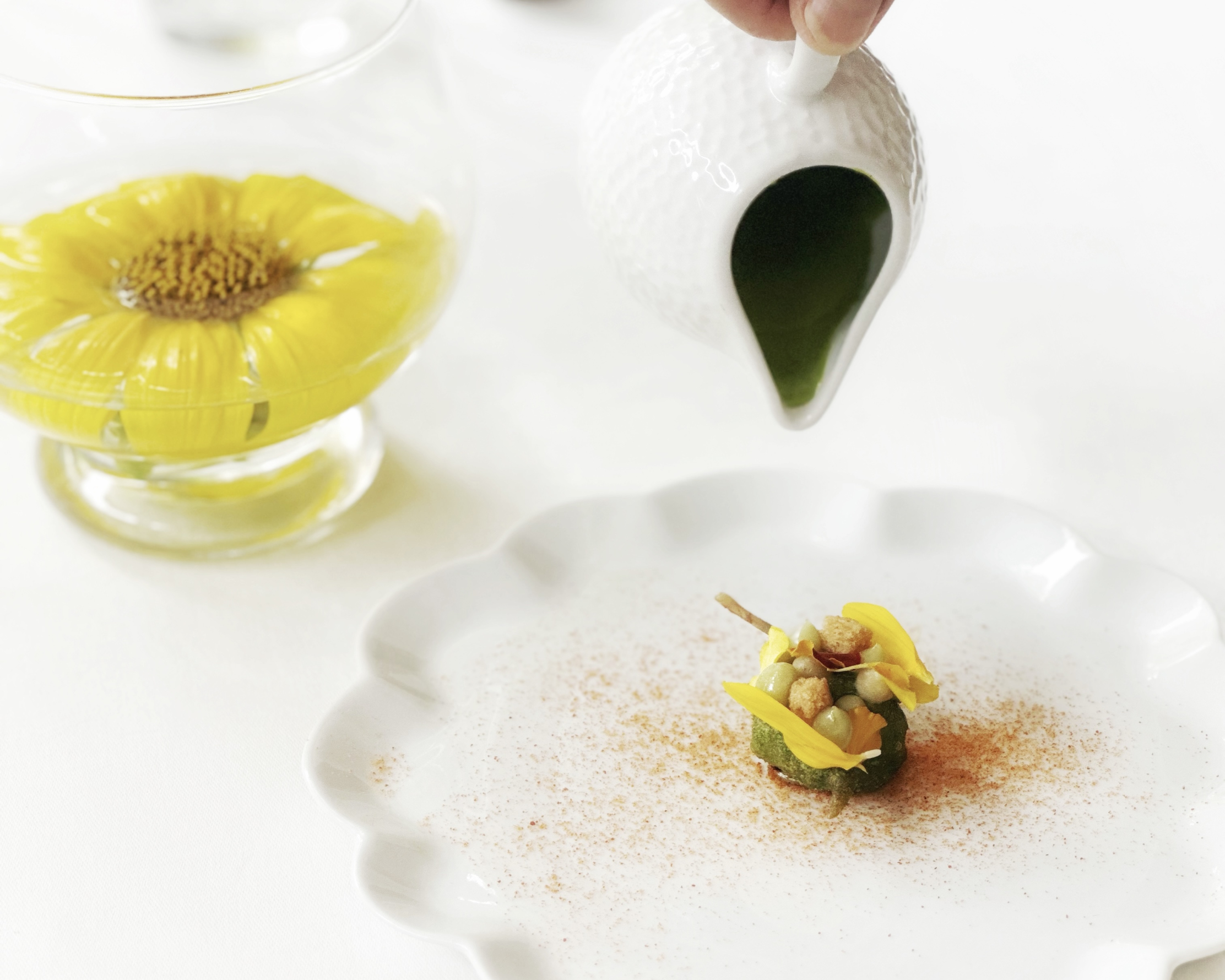 Plat gastronomique raffiné servi au restaurant L'Olivier dans le Luberon, décoré de fleurs comestibles jaunes et accompagné d'une sauce verte.